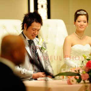 披露宴で来賓のスピーチを聞く新郎と新婦